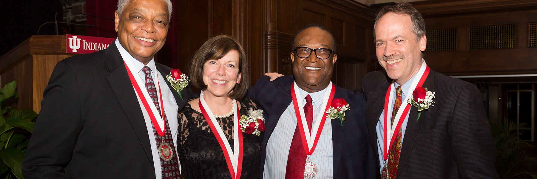 A brown haired woman stands smiling between two African American men in suits—all wearing medals